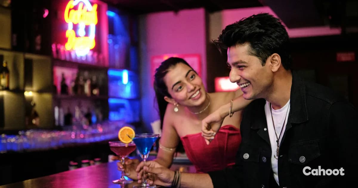 A smiling couple enjoying cocktails at a neon-lit bar